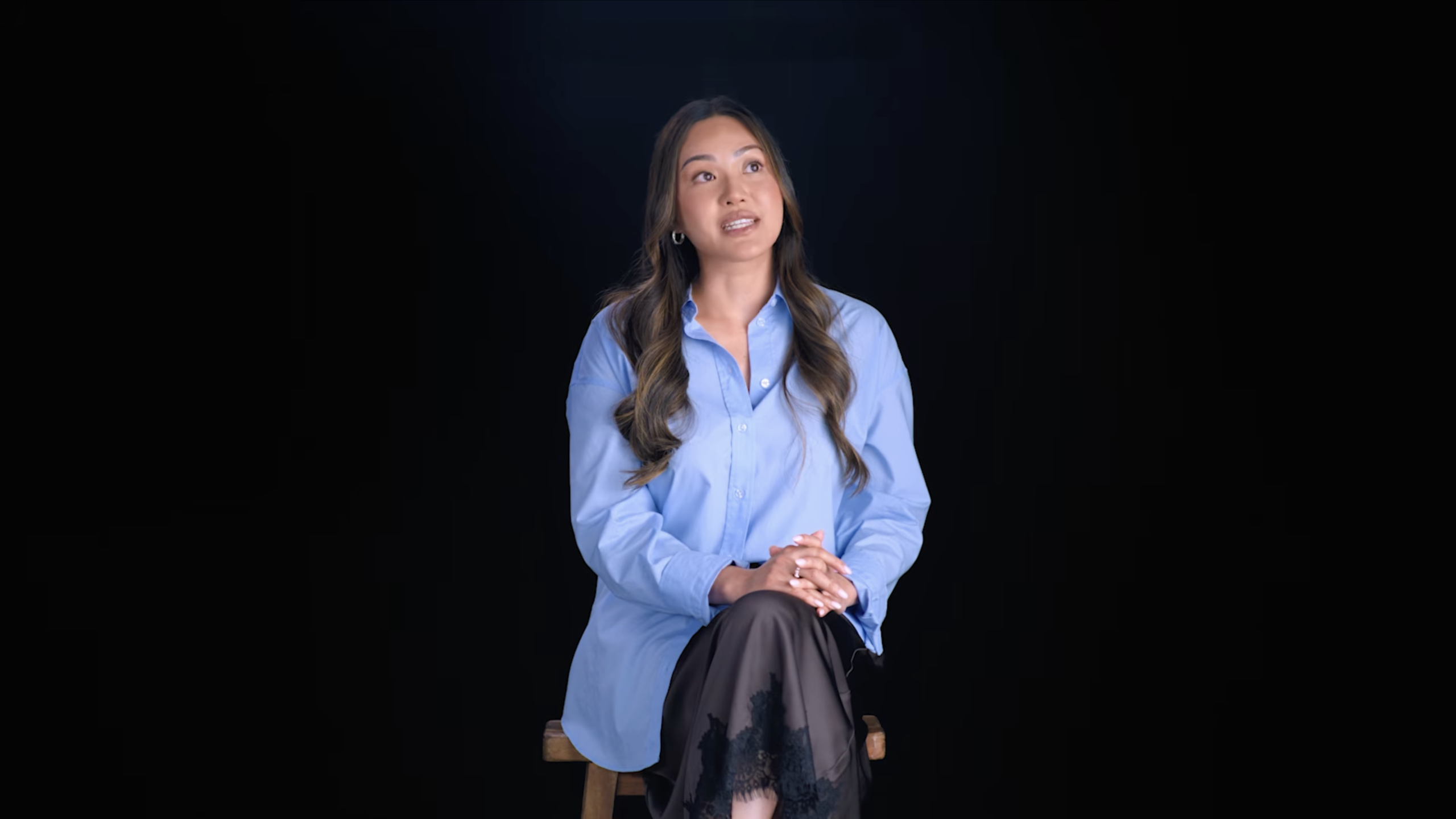 A patient in a blue shirt, seated on a stool, shares her story against a black backdrop, Victoria Park Medispa campaign