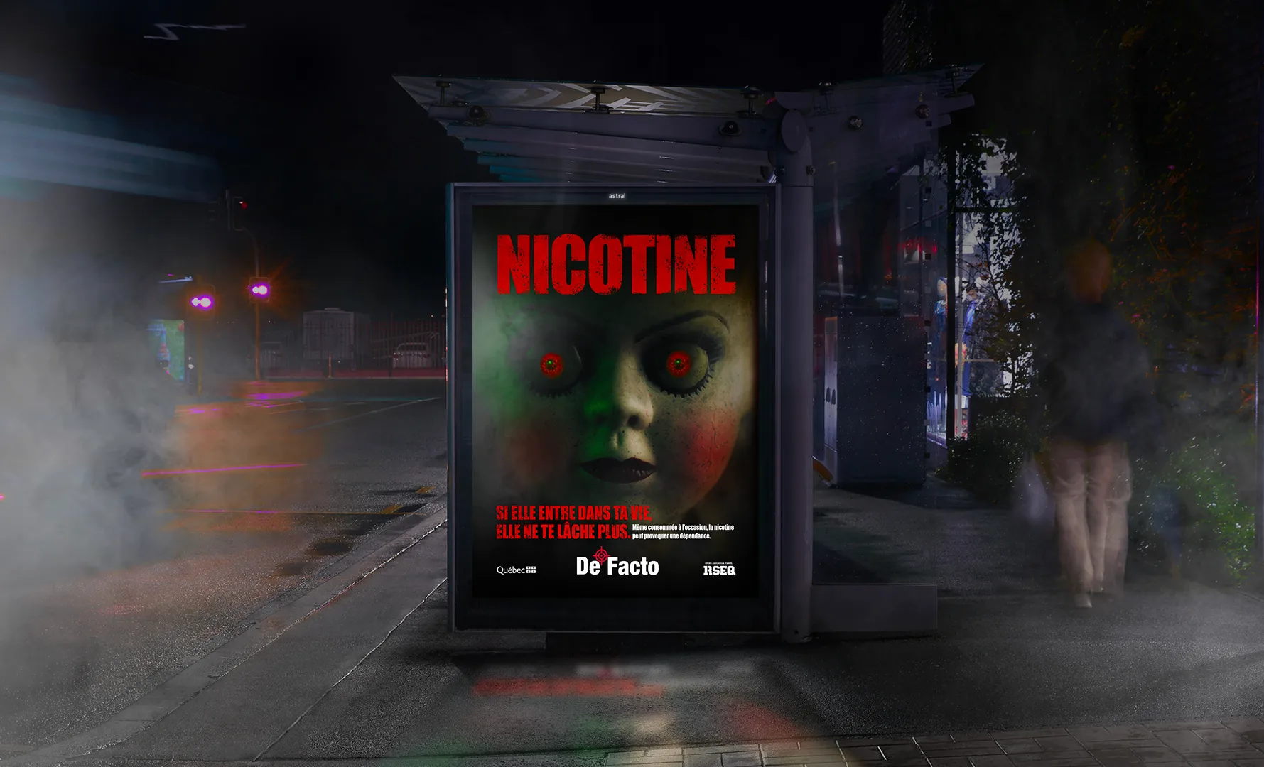 Abribus de nuit dans la fumée, avec l’affiche « Nicotine » de la poupée aux yeux rouges, campagne De Facto du RSEQ
