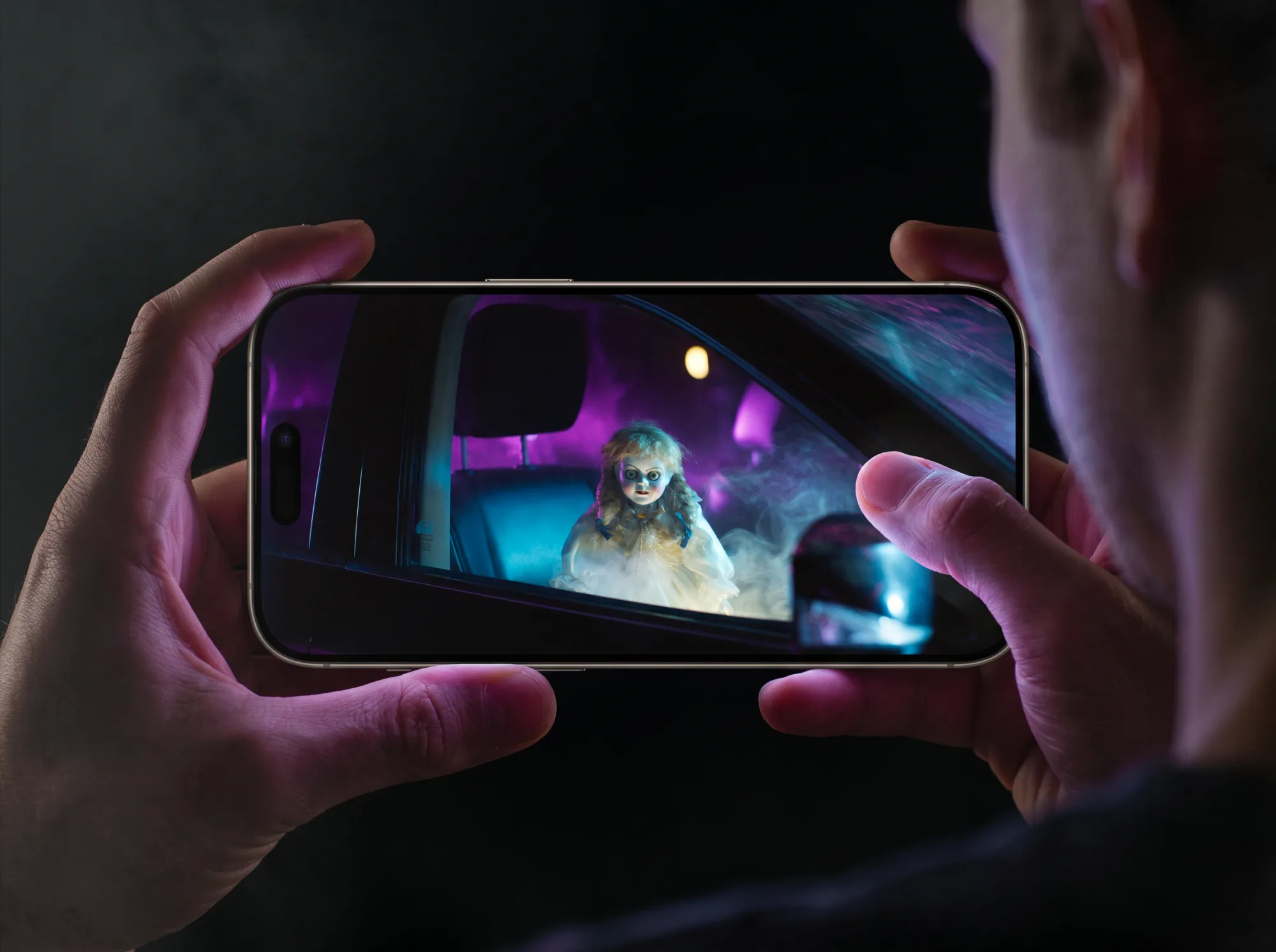 Des mains tiennent un téléphone qui montre une poupée assise dans une voiture, sous une lumière violette, image tirée du film
