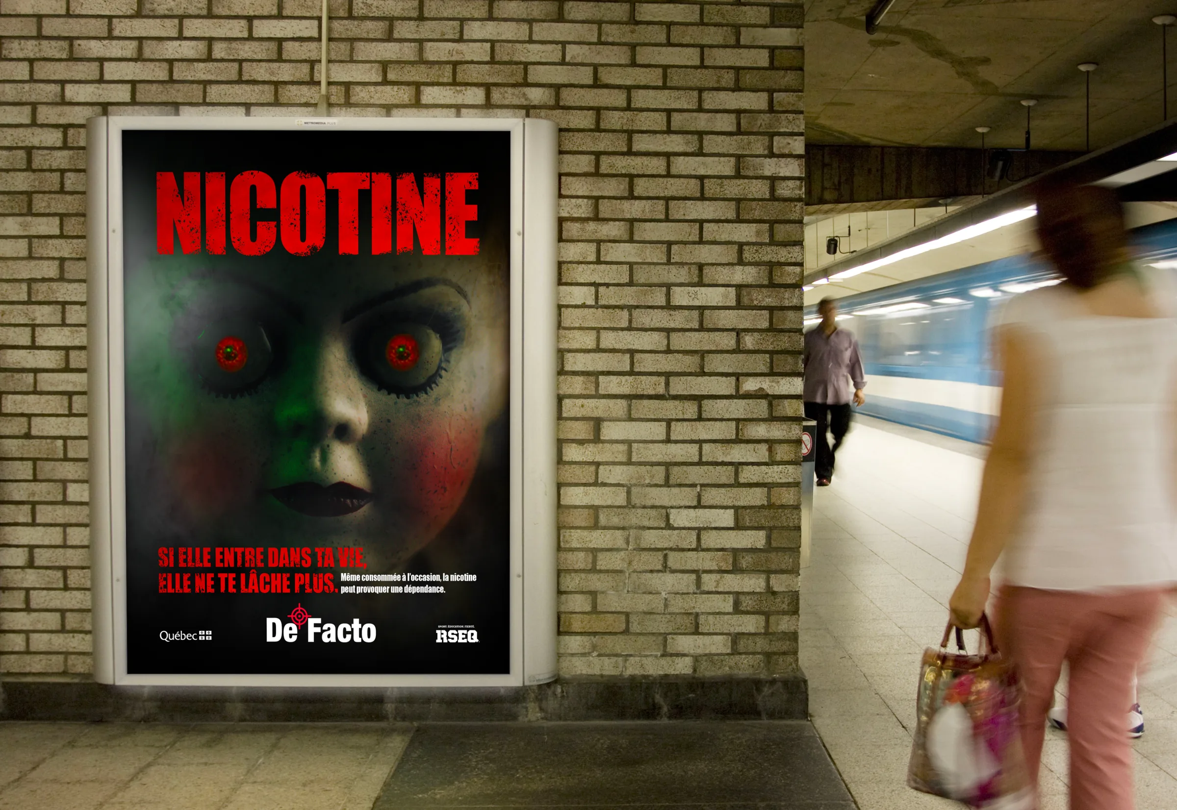 Affiche « Nicotine » de la poupée aux yeux rouges sur le mur de briques d’une station de métro, une voyageuse passe